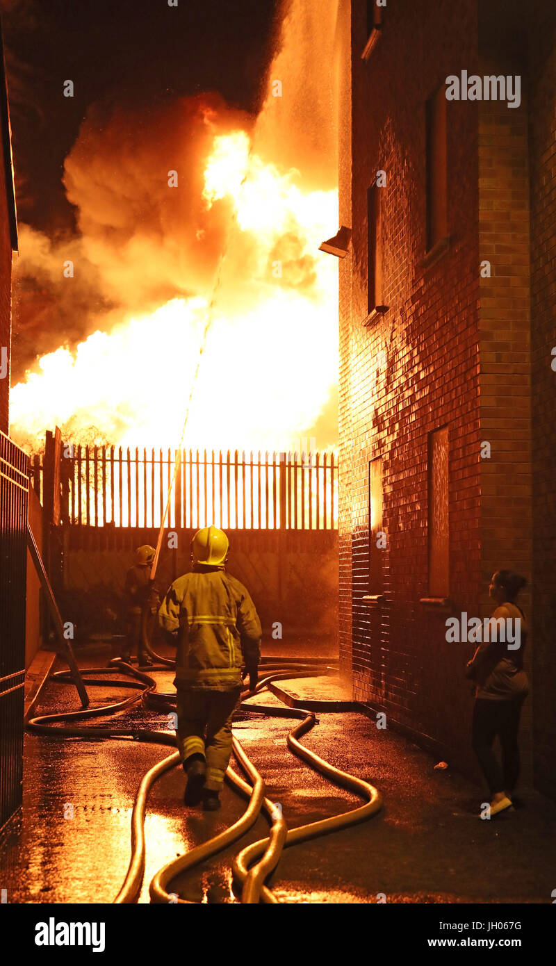 Vigili del fuoco smorzare vicino casa come un falò a Ravenscroft Avenue a Belfast è accesa prima della data chiave nella protestante ordine leale marching stagione - il dodicesimo di luglio. Foto Stock