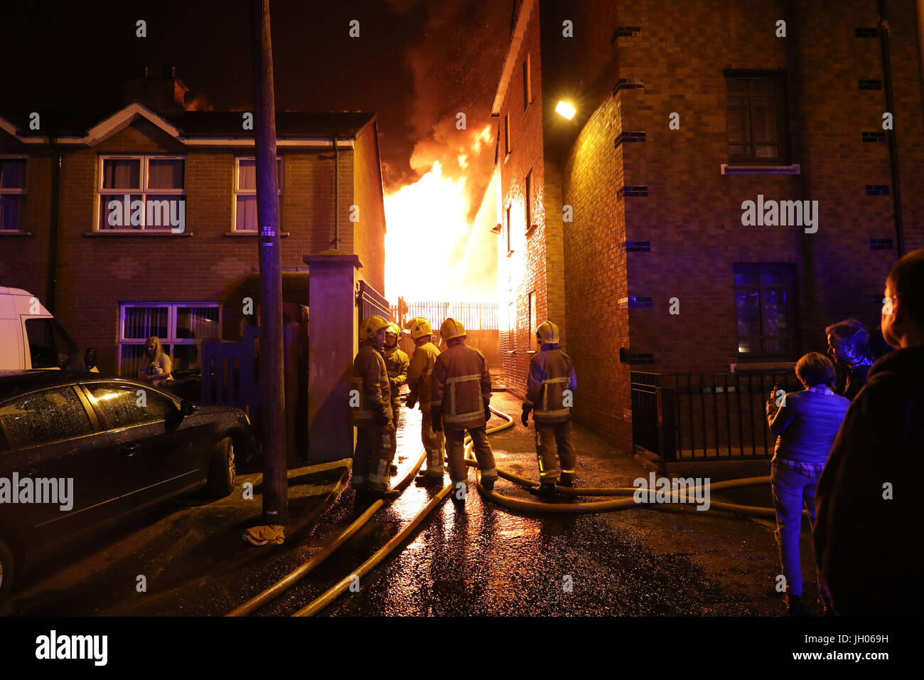 Vigili del fuoco smorzare vicino casa come un falò a Ravenscroft Avenue a Belfast è accesa prima della data chiave nella protestante ordine leale marching stagione - il dodicesimo di luglio. Foto Stock
