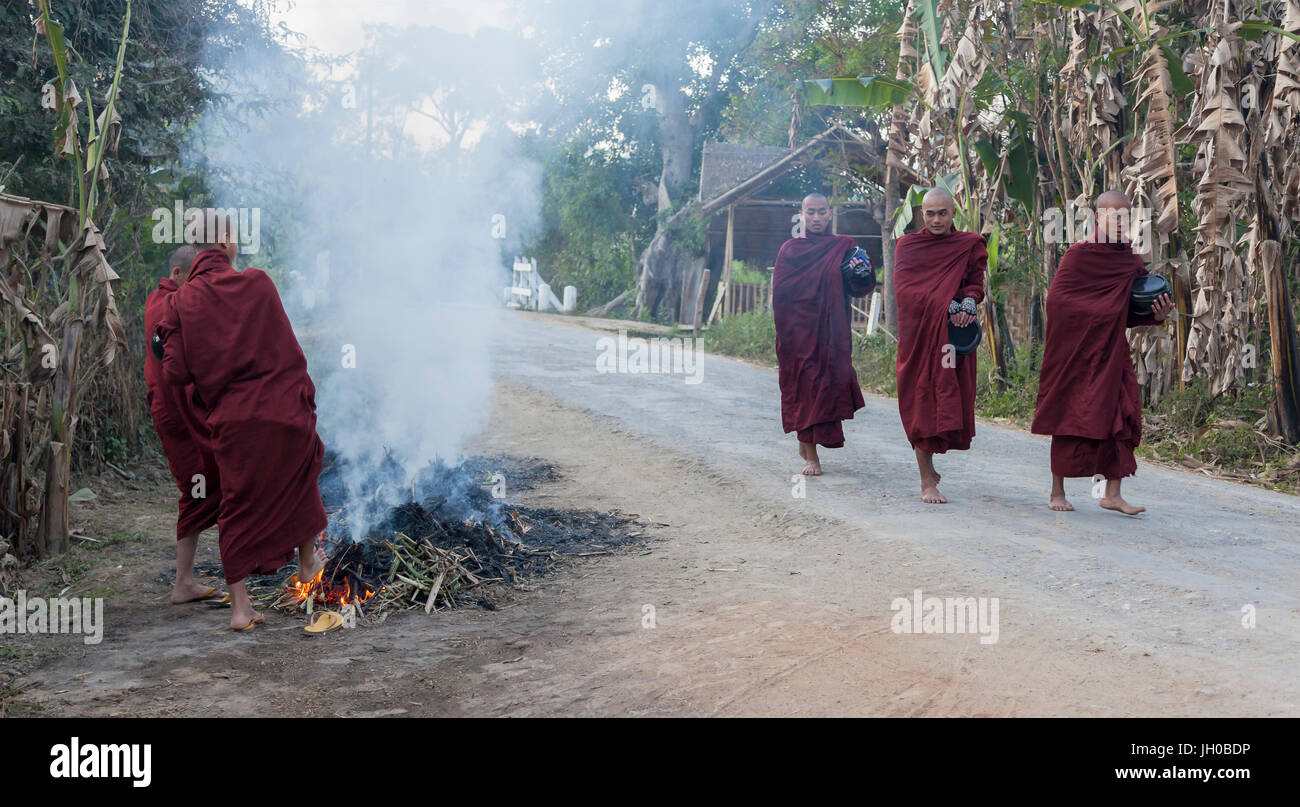 I monaci birmani riscaldando i loro piedi sulla strada Foto Stock