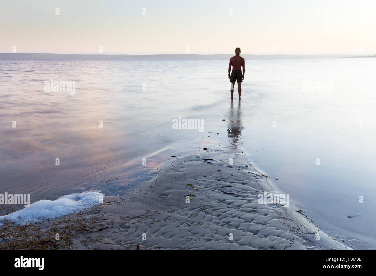 Un uomo si erge, stagliano contro una bella, setoso calma oceano. Foto Stock