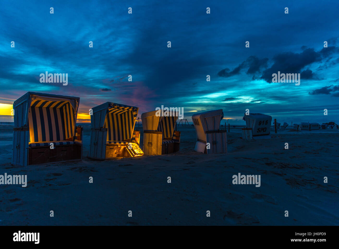 Twilight presso la spiaggia di affondò Peter Ording in Germania del nord. Sedie da spiaggia sono dolci illuminato da luci durante la tempesta set di Sun Foto Stock