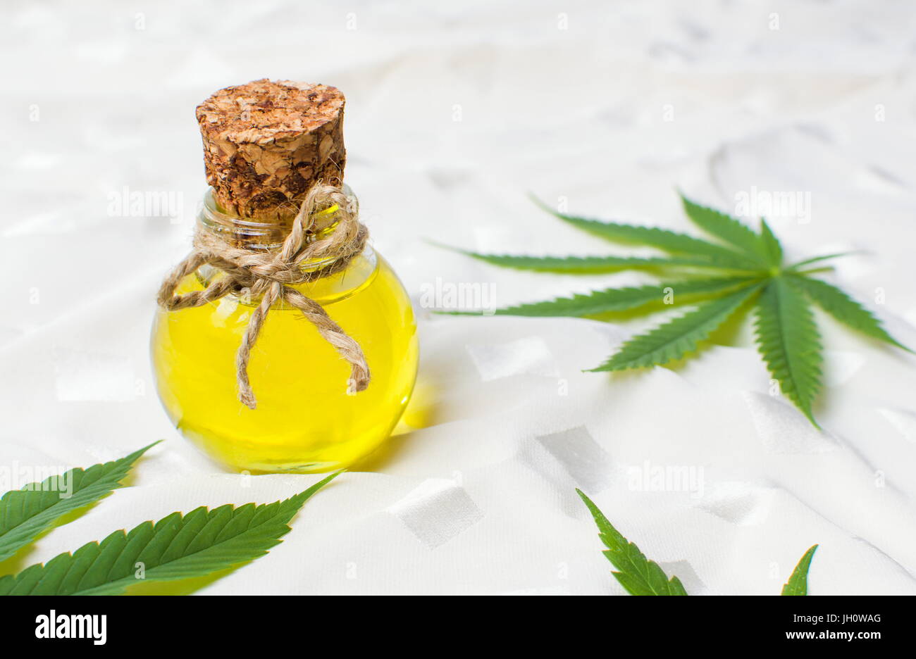 Olio di cannabis e foglie di marijuana sul tessuto bianco Foto Stock
