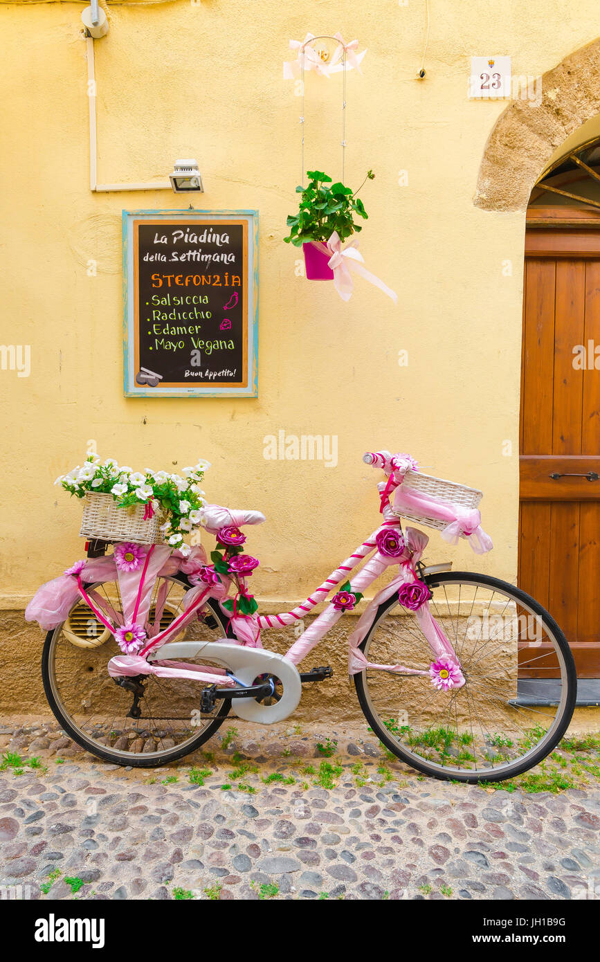 Noleggio mediterraneo, decorate luminosamente bike si appoggia contro una coloratissima parete ristorante nel quartiere della città vecchia di Alghero, Sardegna settentrionale. Foto Stock
