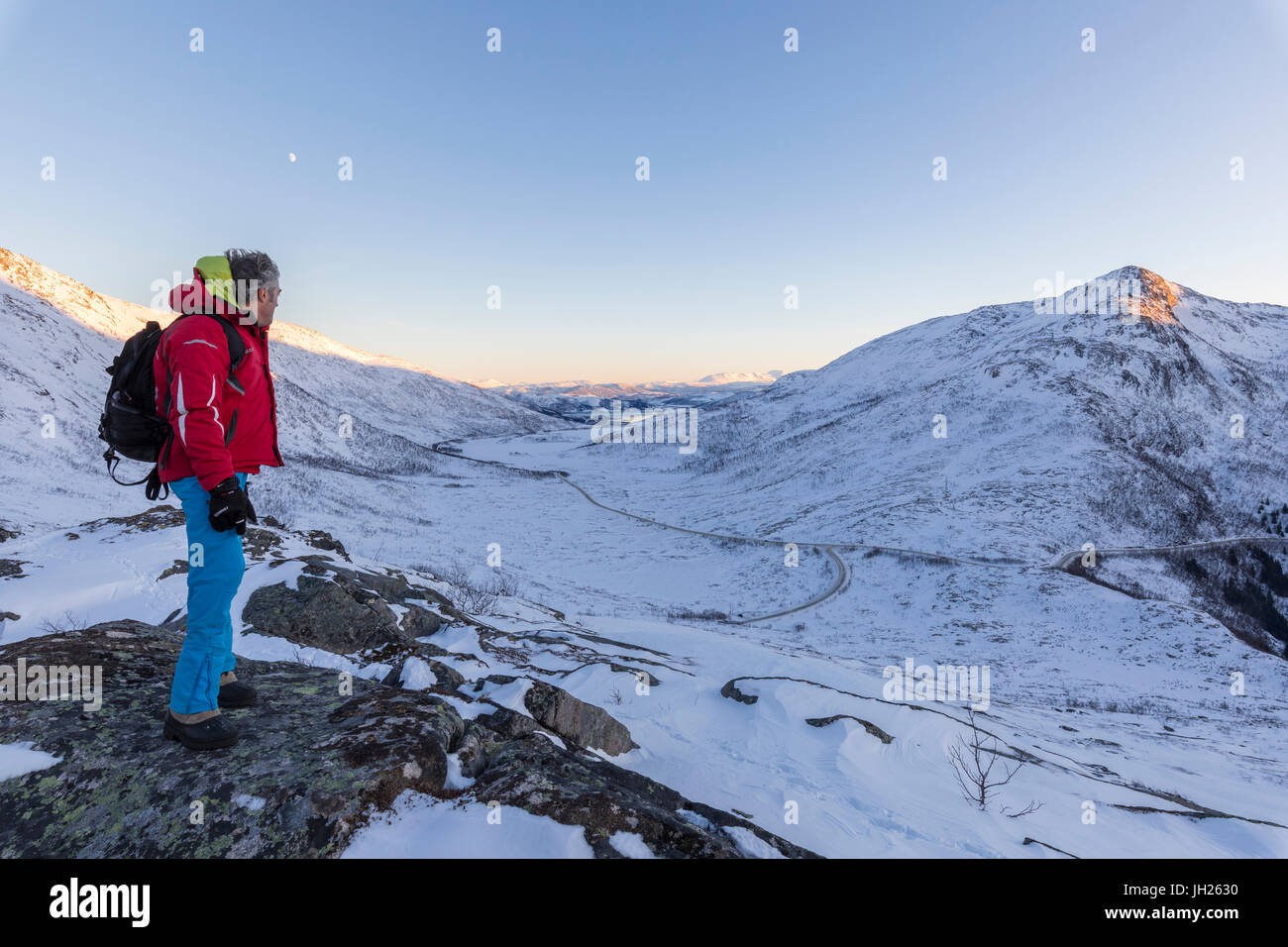 Escursionista sulla parte superiore della cresta rocciosa Ammira le cime innevate di Fjordbotn, Lysnes, Senja, Troms, Norvegia, Scandinavia, Europa Foto Stock