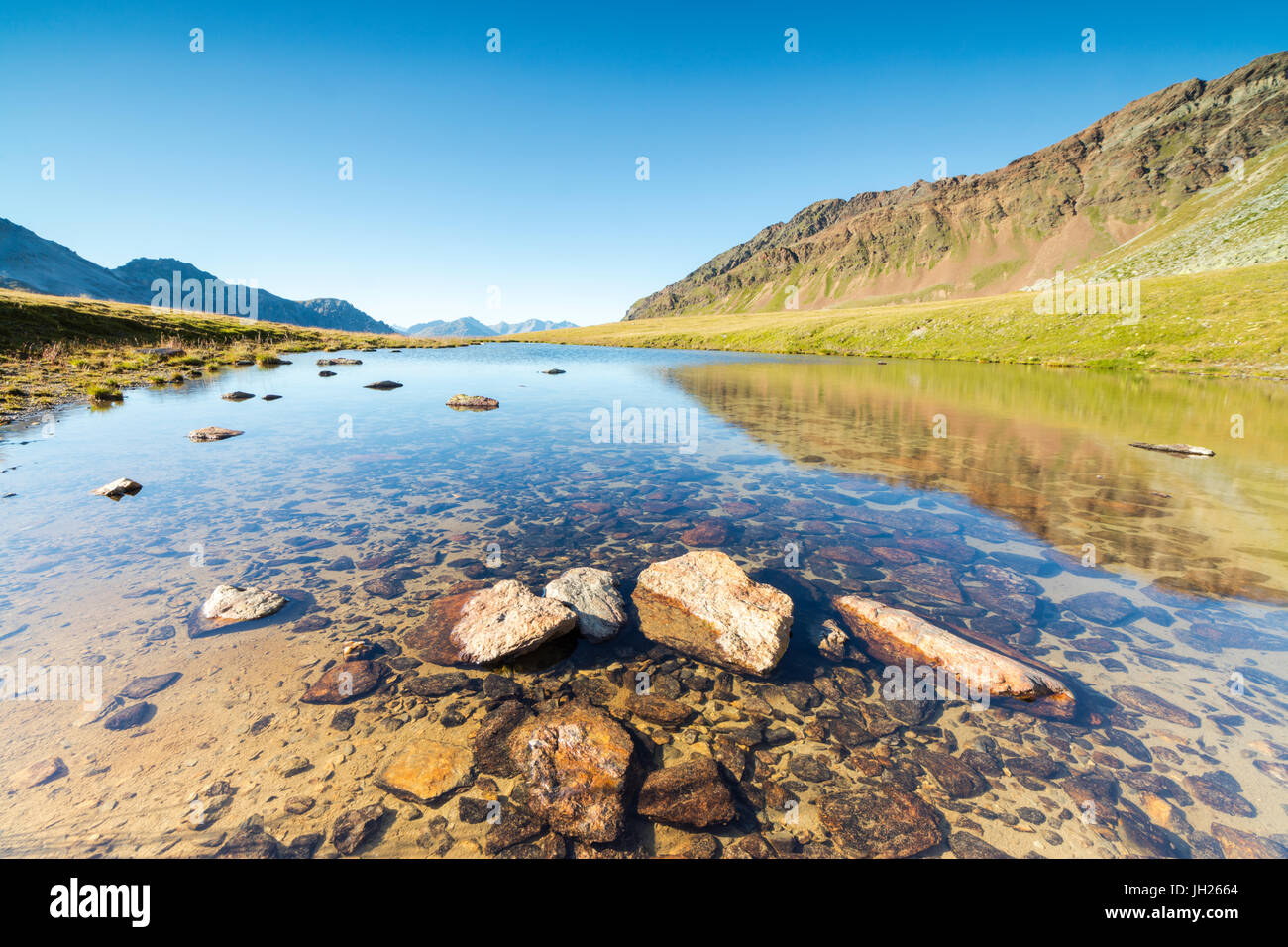Sole splende sui picchi rocciosi si riflette nelle limpide acque del lago Umbrail, Passo Stelvio, Valtellina, Lombardia, Italia, Europa Foto Stock