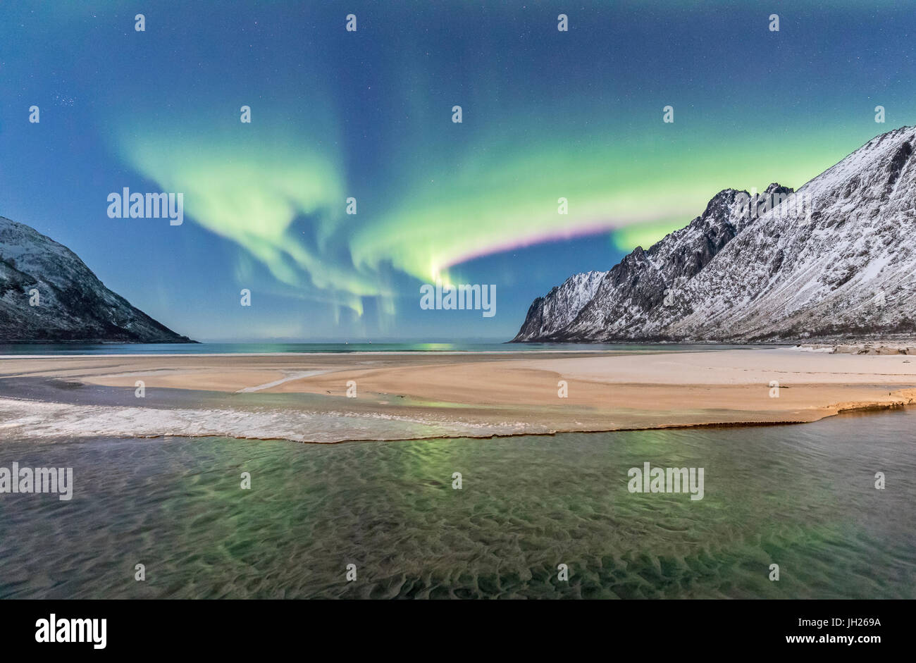 Luci verdi di Northern Lights riflessa nel freddo mare circondato da vette innevate, Ersfjord, Senja, Troms, Norvegia Foto Stock