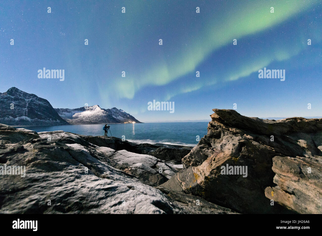 Fotografo sotto le stelle e Northern Lights circondato da picchi rocciosi e mare ghiacciato, Tungeneset, Senja, Troms, Norvegia Foto Stock