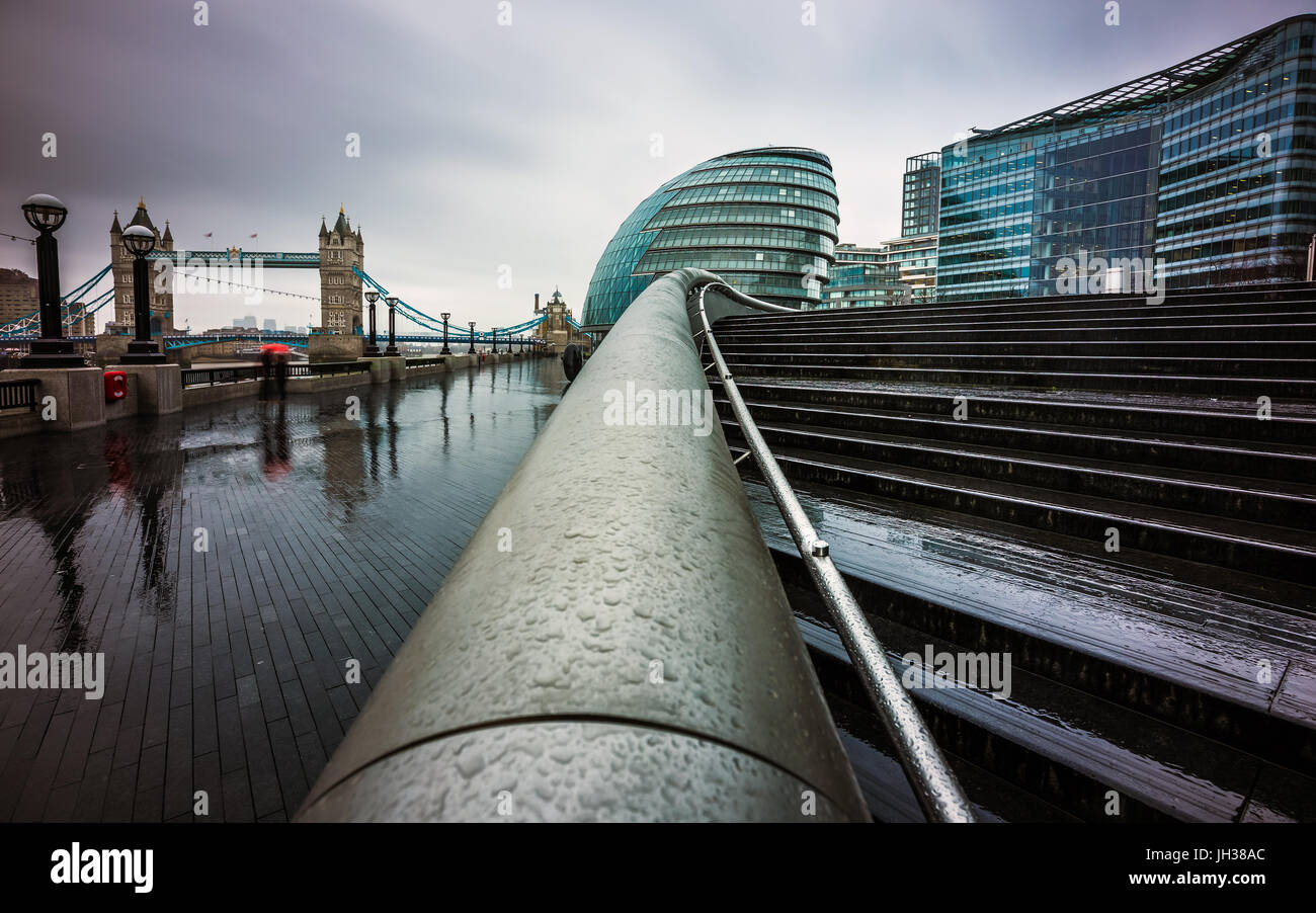 Londra, Inghilterra - Dark Rainy day nel centro di Londra con edifici di uffici e il Tower Bridge e ombrellone rosso a sfondo Foto Stock