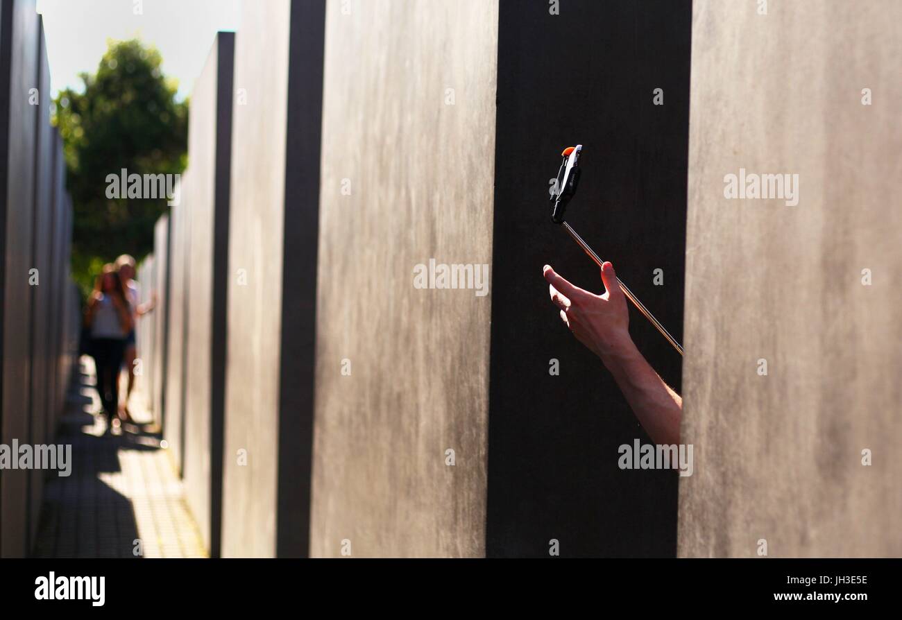 Un turista inglese (invisibile) tenendo un selfie stick con uno smartphone come essa si erge tra le pietre del Monumento all'assassinato ebrei d'Europa (Memoriale dell Olocausto) nel centro di Berlino del giugno 18, 2017 e prende le foto. Questa immagine è parte di una serie di utilizzo | in tutto il mondo Foto Stock