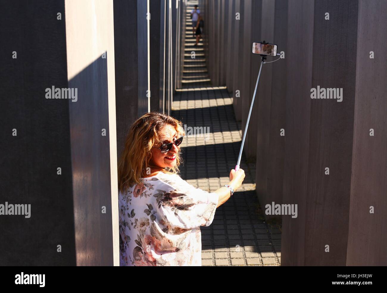 Un italiano turista femminile tenendo un selfie stick con uno smartphone come essa si erge tra le pietre del Monumento all'assassinato ebrei d'Europa (Memoriale dell Olocausto) nel centro di Berlino del giugno 18, 2017 e prende le foto. Questa immagine è parte di una serie o di utilizzo | in tutto il mondo Foto Stock