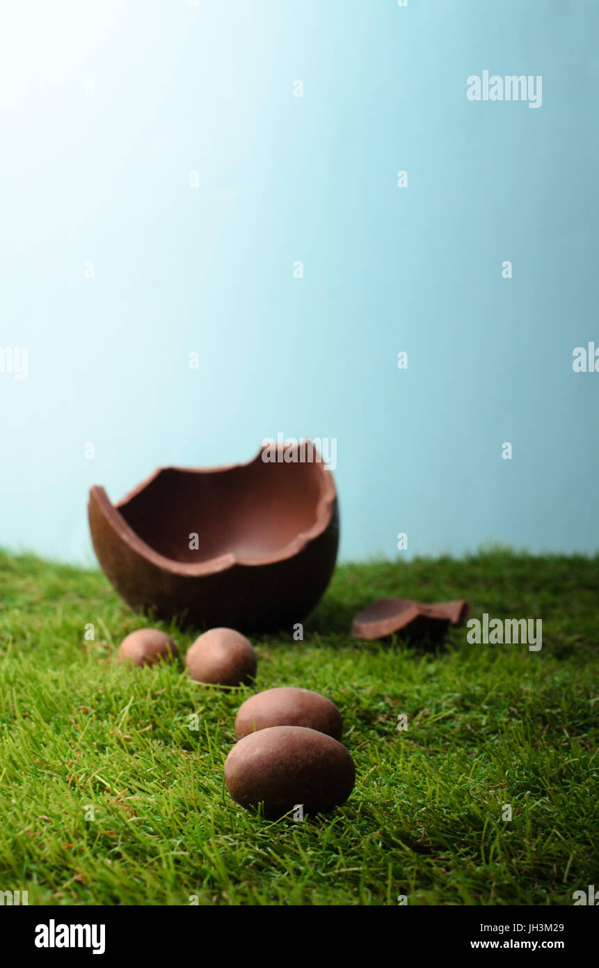 Pasqua in scena con il piccolo latte uova di cioccolato formando un percorso di una collina erbosa , portando ad un uovo di grandi dimensioni che è spezzato. Cielo blu dietro e al di sopra Foto Stock
