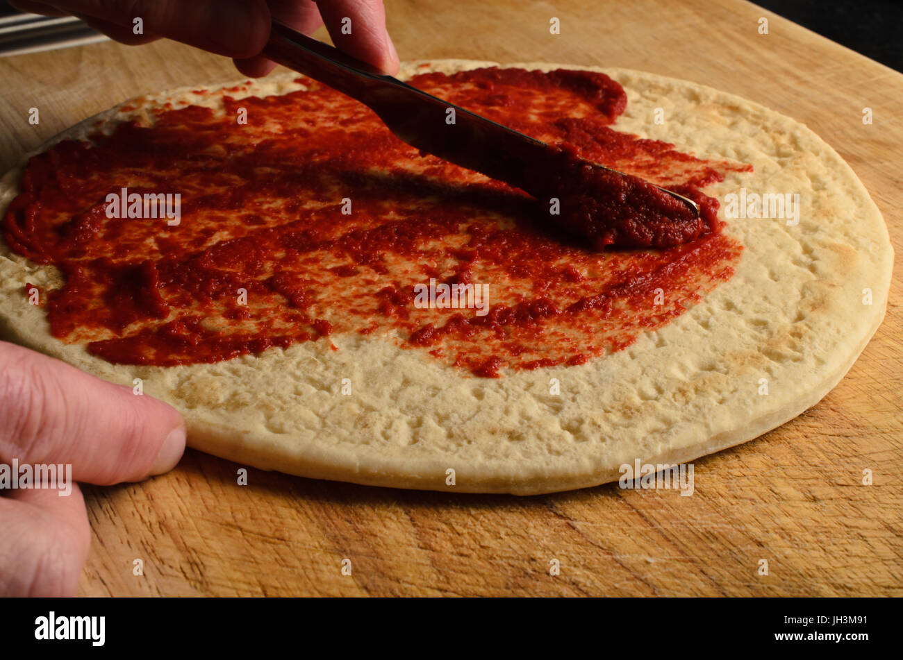 Maschio di spargimento a mano base di pomodoro sopra la pizza sul usurati, graffiati tagliere di legno. Illuminazione scuro. Foto Stock