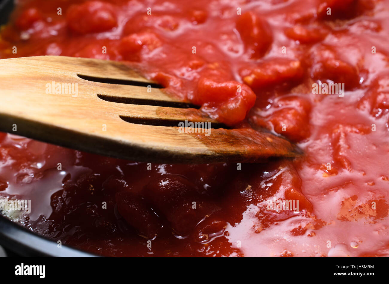 Il gorgogliamento hot salsa di pomodoro per la pasta, la cottura in pentola con una spatola di legno. Foto Stock