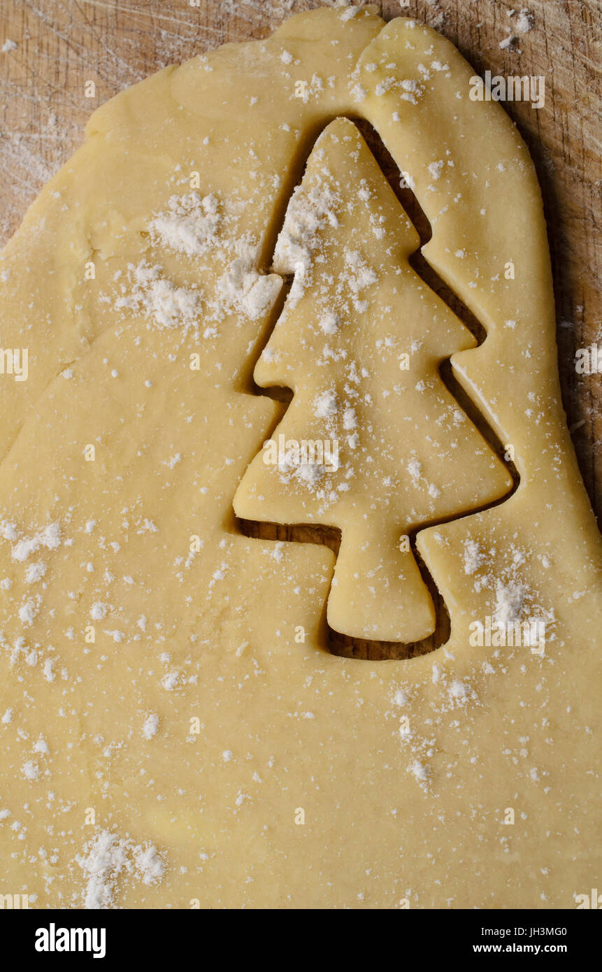 Biscotti di Natale o cookie rendendo concetto con albero di Natale forma tagliata di impasto arrotolato. Un pizzico di farina in pasticceria e tavola di legno al di sotto. Foto Stock