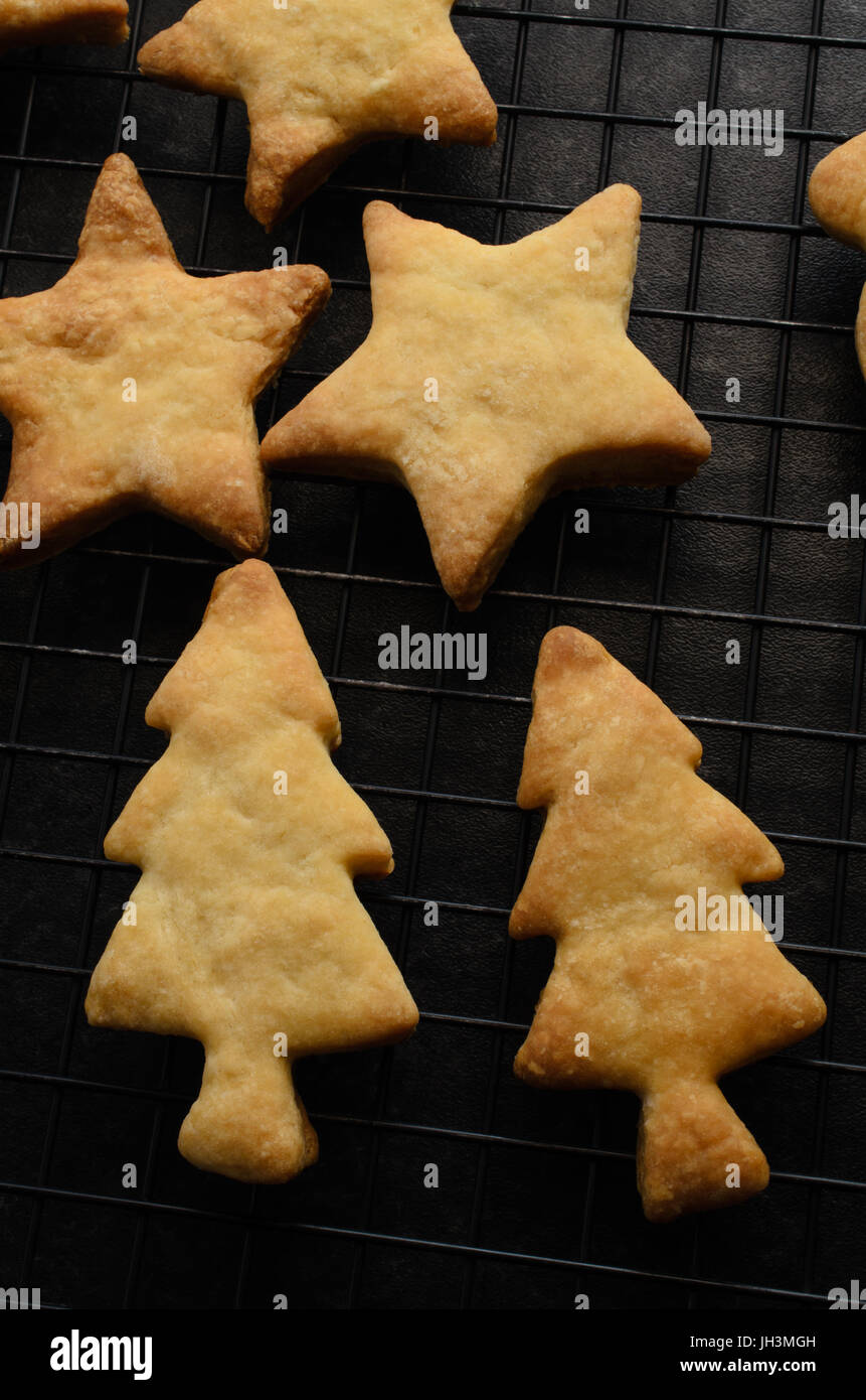 Scatto dall'alto di una selezione di biscotti di Natale nella struttura ad albero e forme stellari, pane appena sfornato e collocato su un filo nero raffreddamento per rack. Foto Stock
