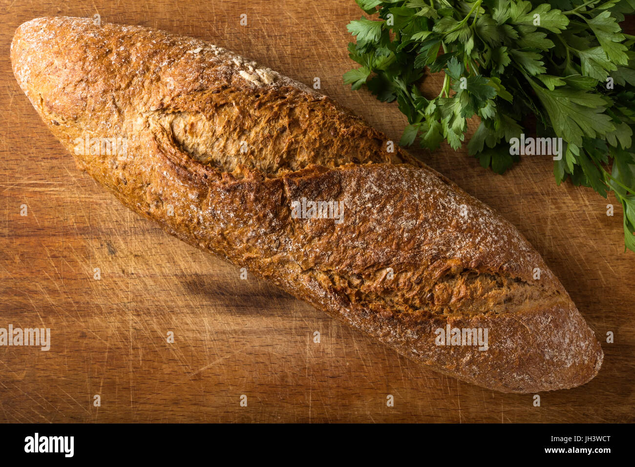 Pane appena sfornato il pane fatto in casa su rustiche in legno scuro dello sfondo con un ciuffo di prezzemolo Foto Stock