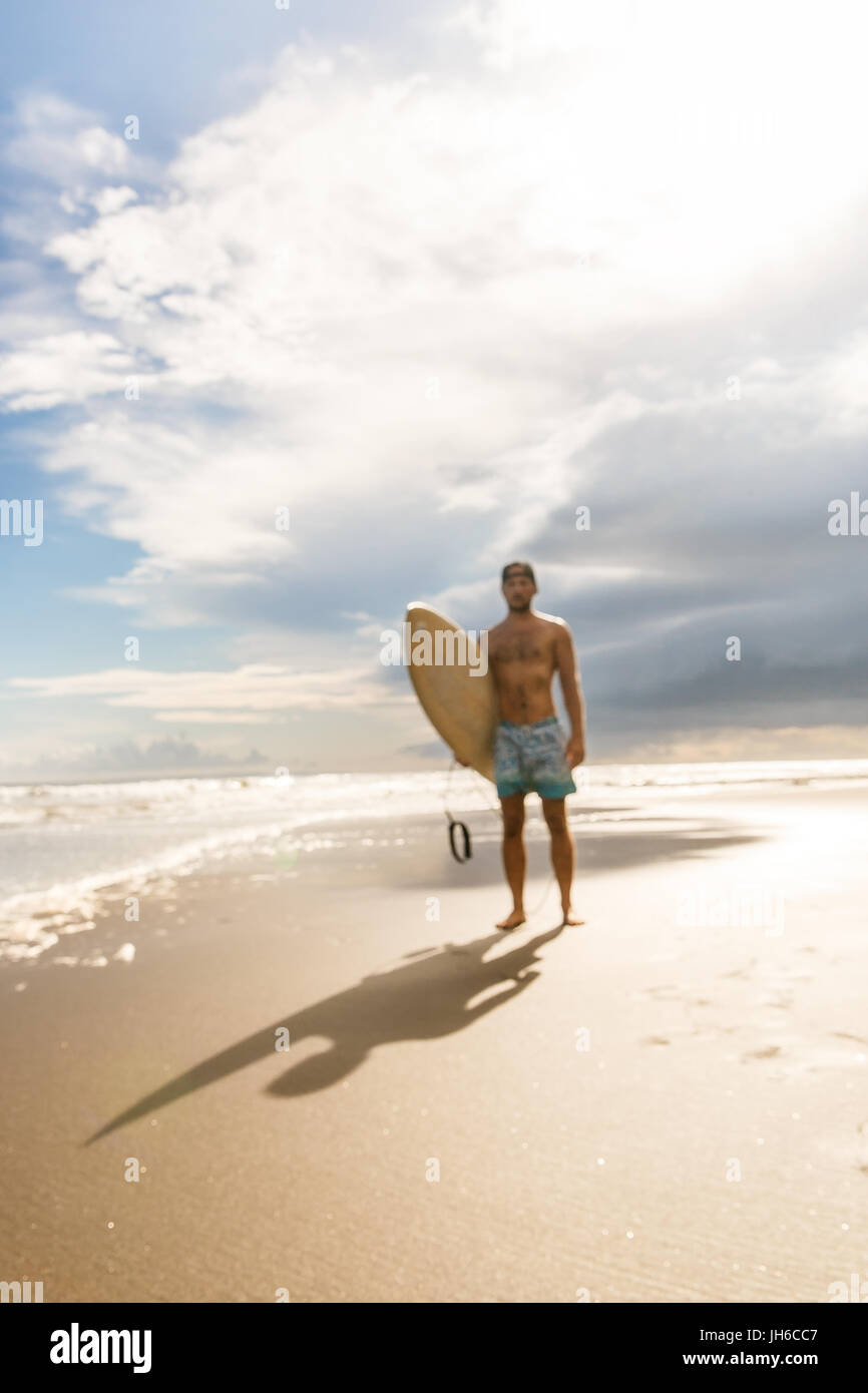 Al di fuori della messa a fuoco, immagini sfocate di bel ragazzo con il surf tavole da surf a piedi dall'acqua al surf spot al mare spiaggia dell'oceano. Concetto di sport, libertà, happine Foto Stock