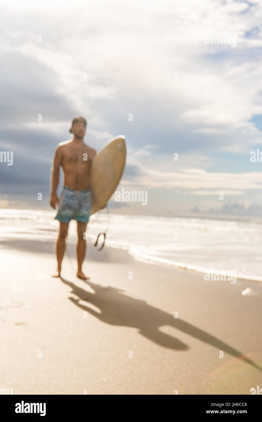Al di fuori della messa a fuoco, immagini sfocate di uomo bello con il surf tavole da surf a piedi dall'acqua al surf spot al mare ocean shore. Concetto di sport, libertà, happine Foto Stock