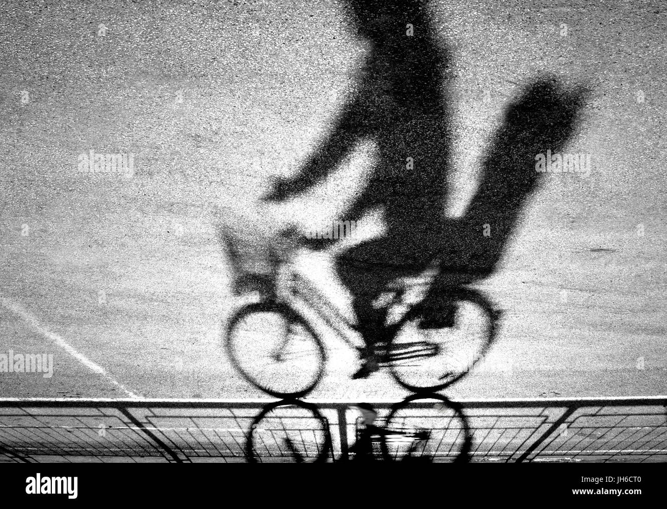 Sfocata ciclista con capretto sedile posteriore silhouette e ombra su un protetto percorso in bicicletta in bianco e nero a testa in giù Foto Stock