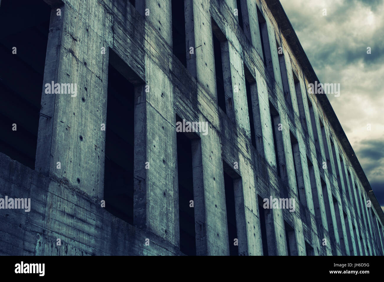 Incompiuta di calcestruzzo abbandonati facciata di edificio con Dark nuvole temporalesche in background Foto Stock