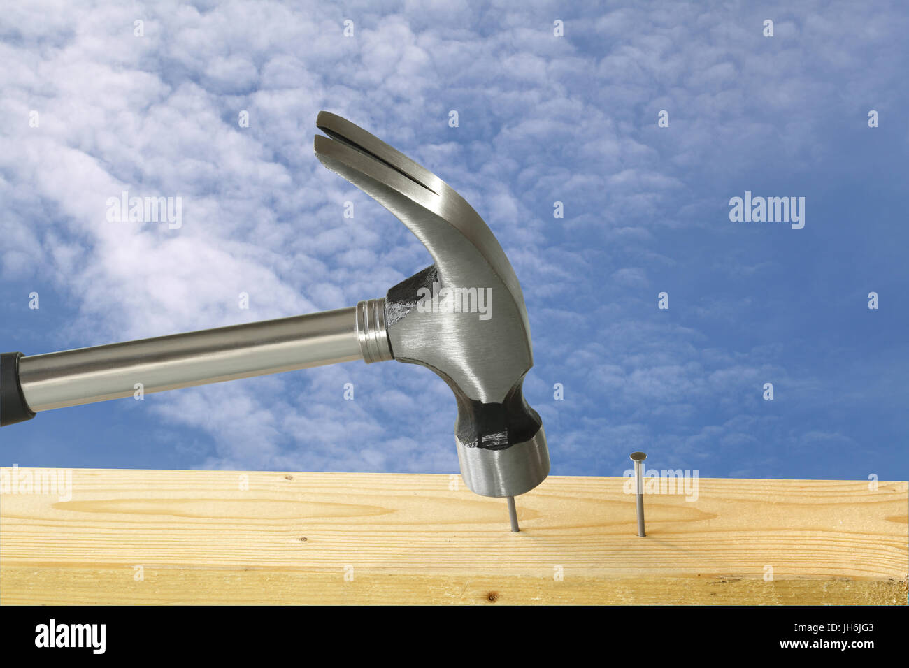 Martello da carpentiere a colpire uno dei due chiodi in un pezzo di legno; mostrato contro un leggermente blu cielo velato, suggerendo un sito di costruzione Foto Stock