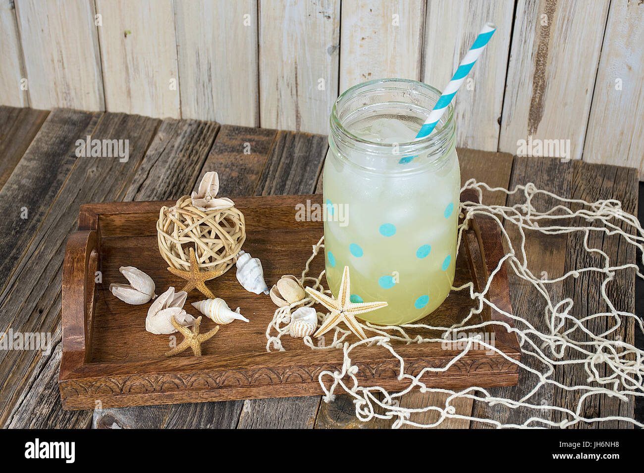 La limonata drink nella polka dot mason jar con paglia a strisce con conchiglie in legno che serve il vassoio Foto Stock