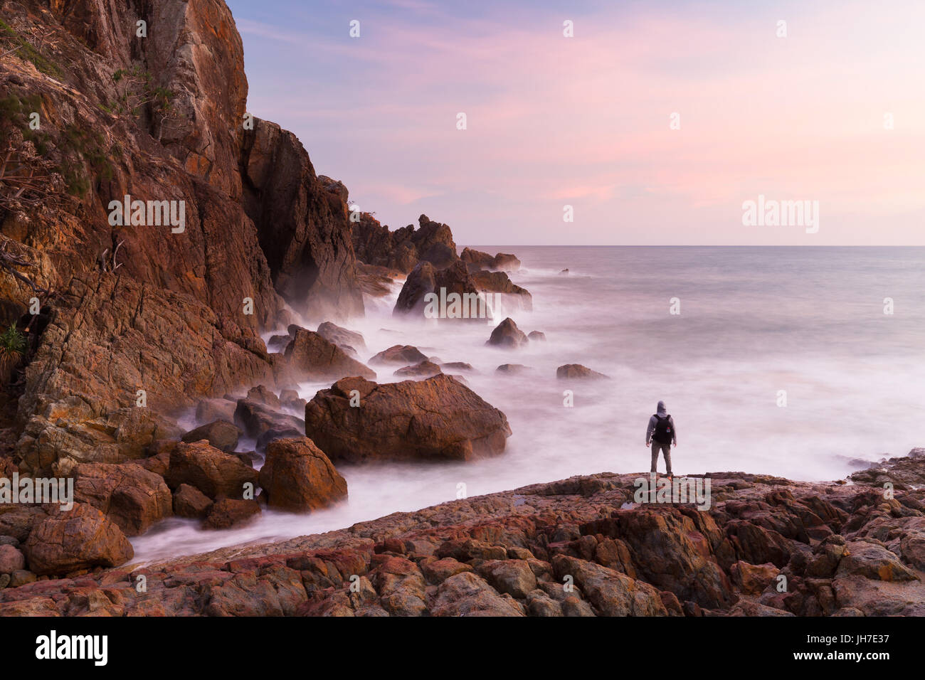 Una persona si profila da una rosa di Alba alla base di una scogliera costiera in un bellissimo paesaggio marino scena. Foto Stock