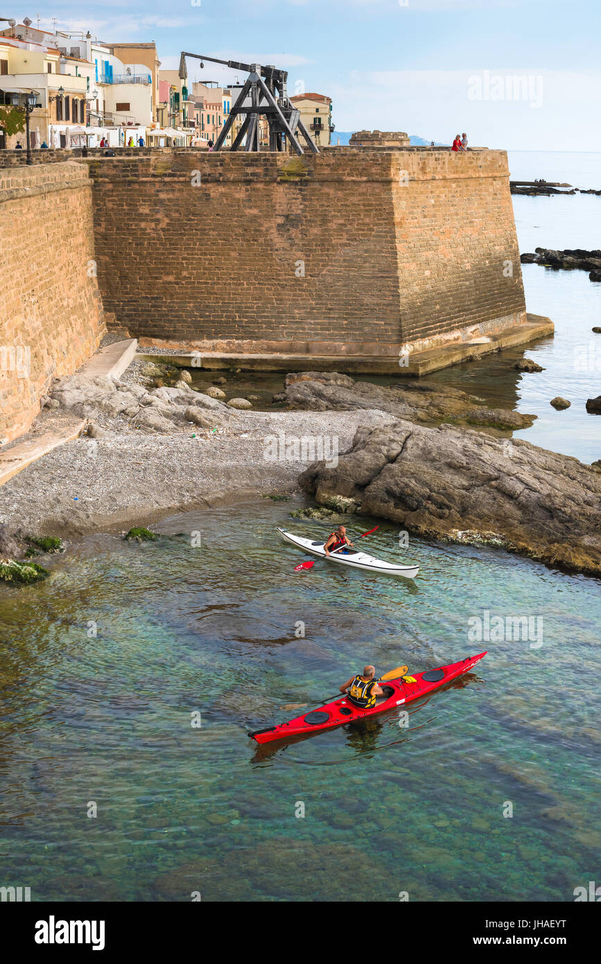 La costa della Sardegna Alghero, dettaglio del medievale seawall - dei Bastioni Marco Polo - con gli uomini paddling loro kayak in primo piano, Alghero Sardegna. Foto Stock