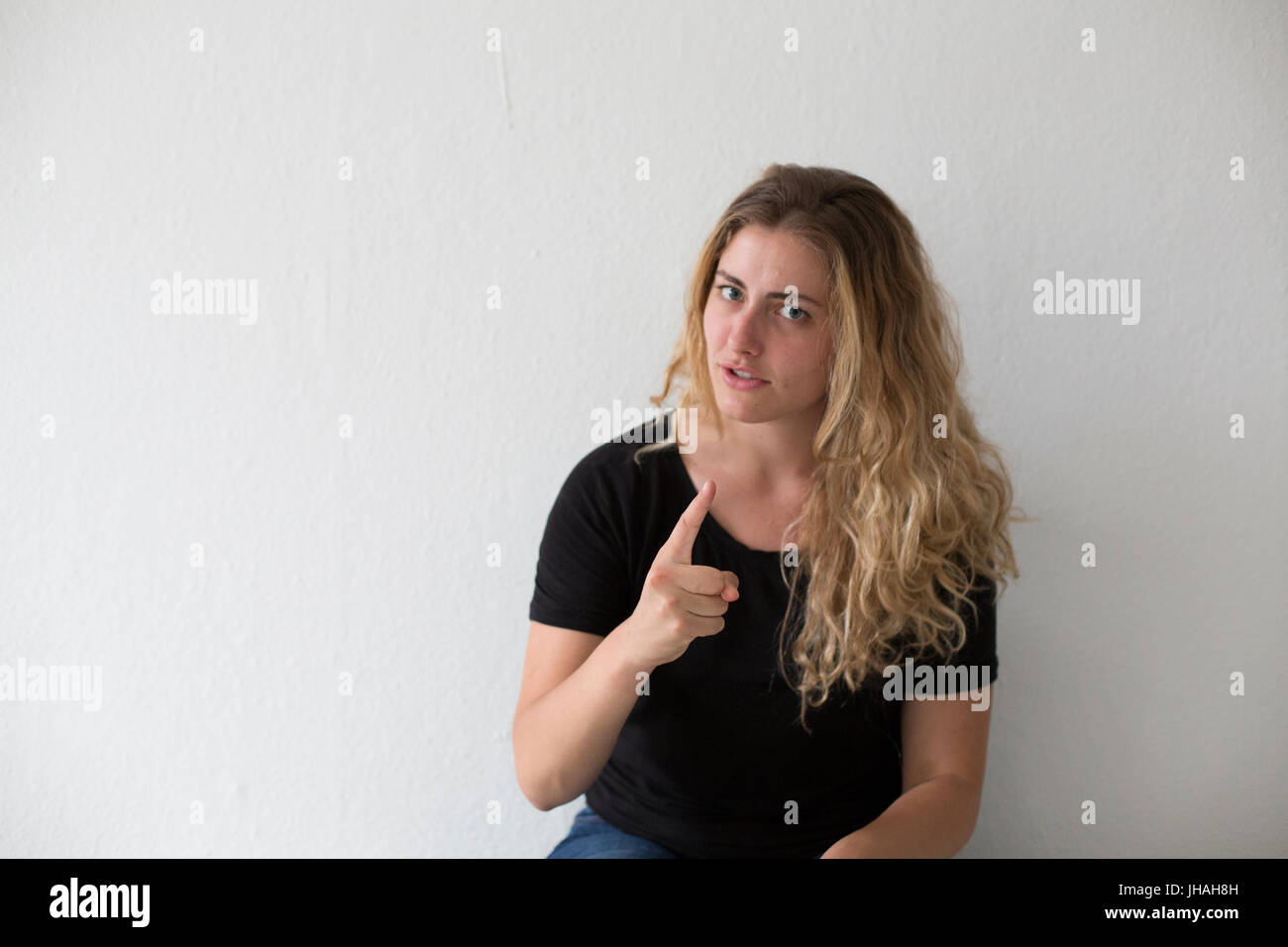 Giovani, bionda, donna caucasica esprime emozioni negative, ira, urlando e puntare il dito al visualizzatore e fotografo su uno sfondo bianco. Foto Stock