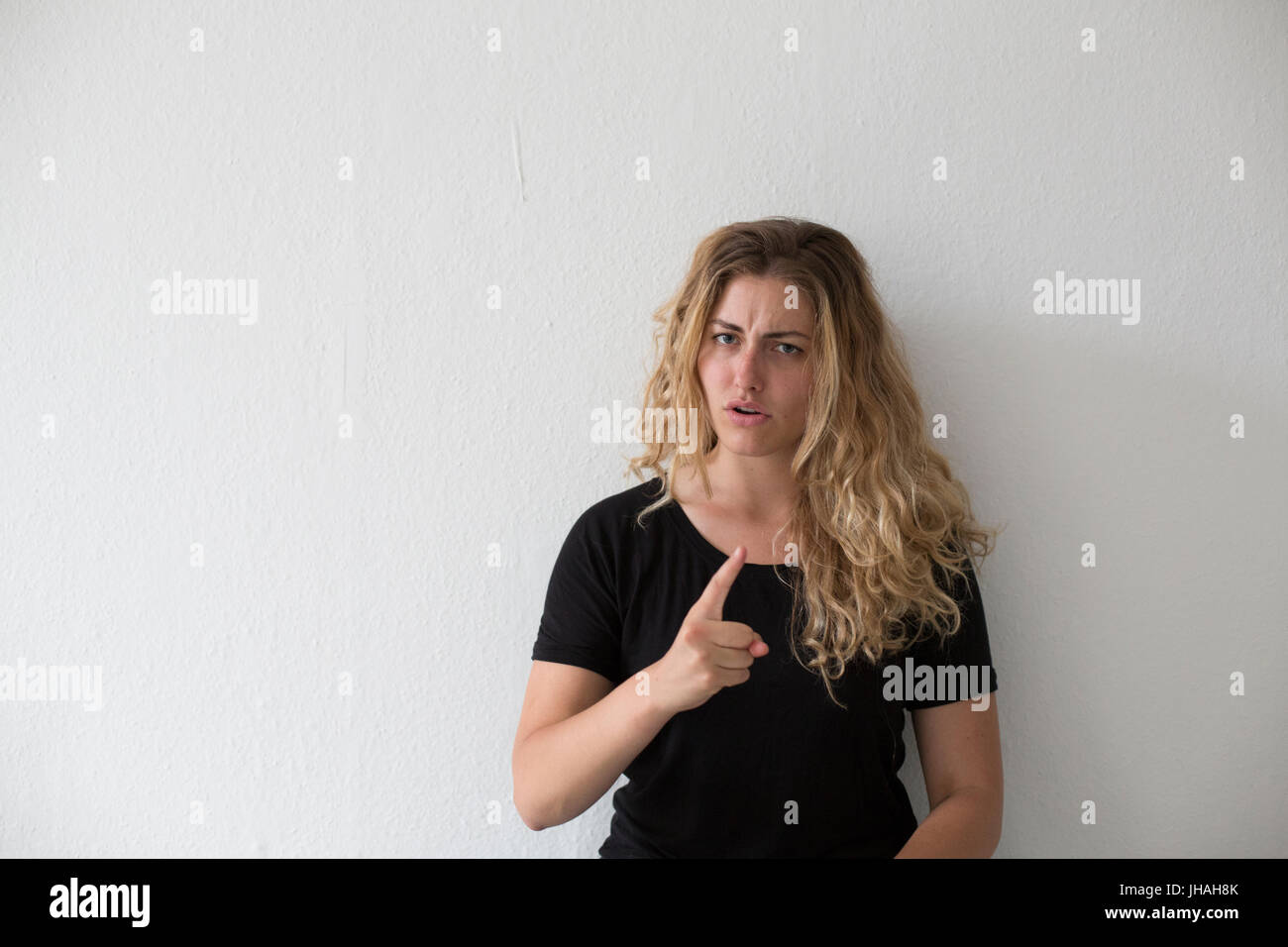 Giovani, bionda, donna caucasica esprime emozioni negative, ira, urlando e puntare il dito al visualizzatore e fotografo su uno sfondo bianco. Foto Stock