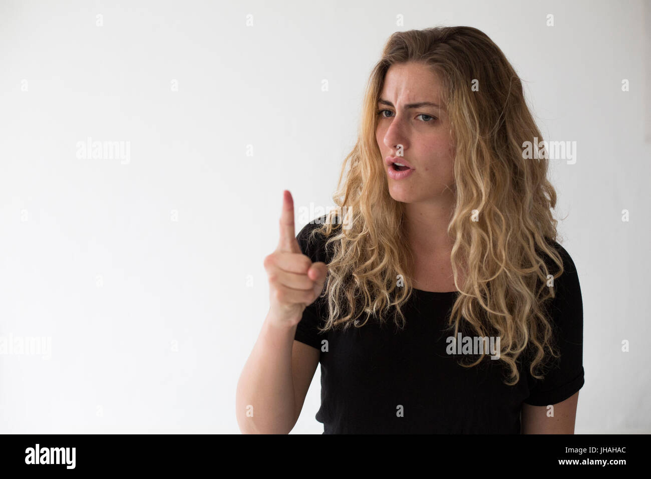 Giovani, bionda, donna caucasica esprime emozioni negative, ira, urlando e puntare il dito al visualizzatore e fotografo su uno sfondo bianco. Foto Stock