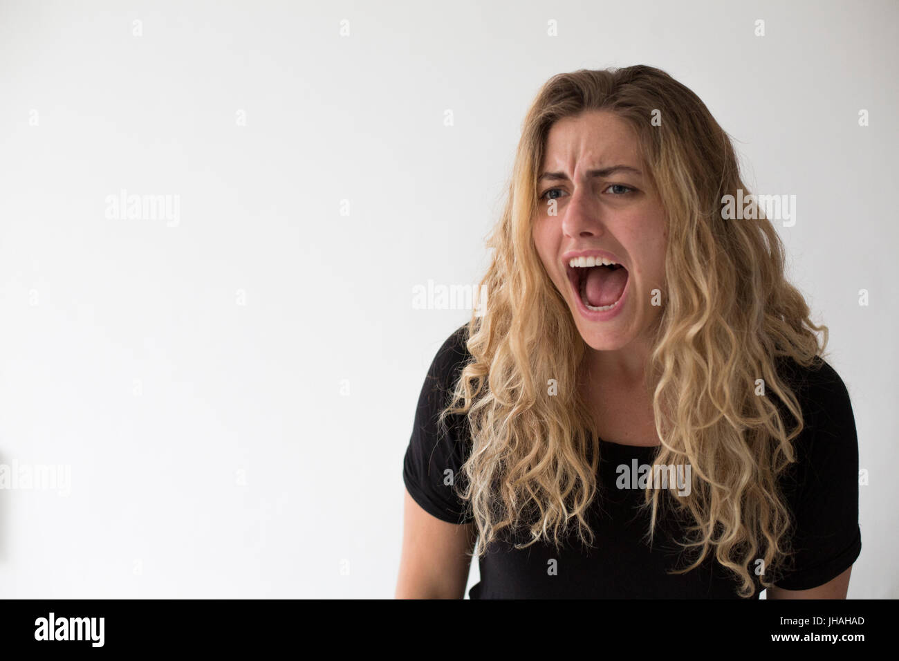 Giovani, bionda, donna caucasica esprime emozioni negative, ira, urlando e puntare il dito al visualizzatore e fotografo su uno sfondo bianco. Foto Stock