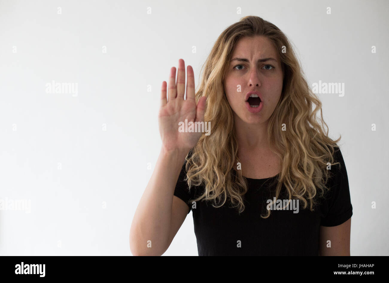 Giovane donna bionda esprime cautela e attenzione viewer non proseguire. Contro uno sfondo bianco stringe la mano fino al visualizzatore. Foto Stock