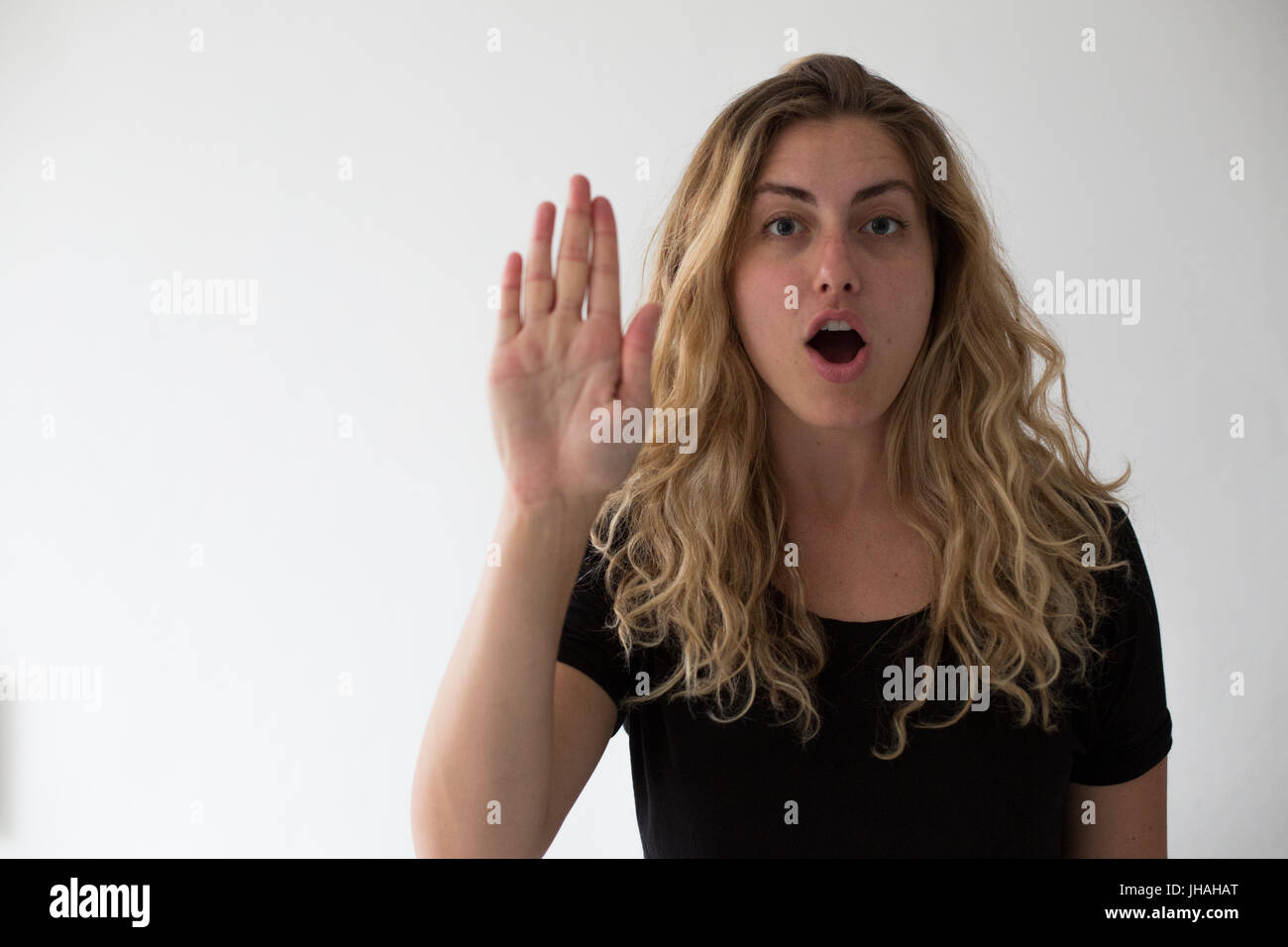 Giovane donna bionda esprime cautela e attenzione viewer non proseguire. Contro uno sfondo bianco stringe la mano fino al visualizzatore. Foto Stock