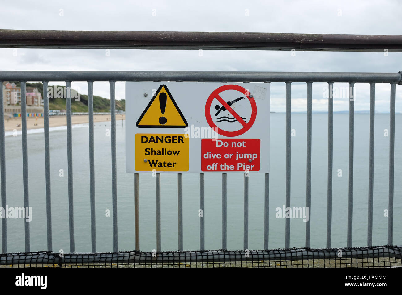 Un segno Attenzione gente di mare poco profondo e acqua e dire alla gente di non tuffarsi o salta fuori il molo (Boscombe pier vicino a Bournemouth in Dorset, Inghilterra). Foto Stock