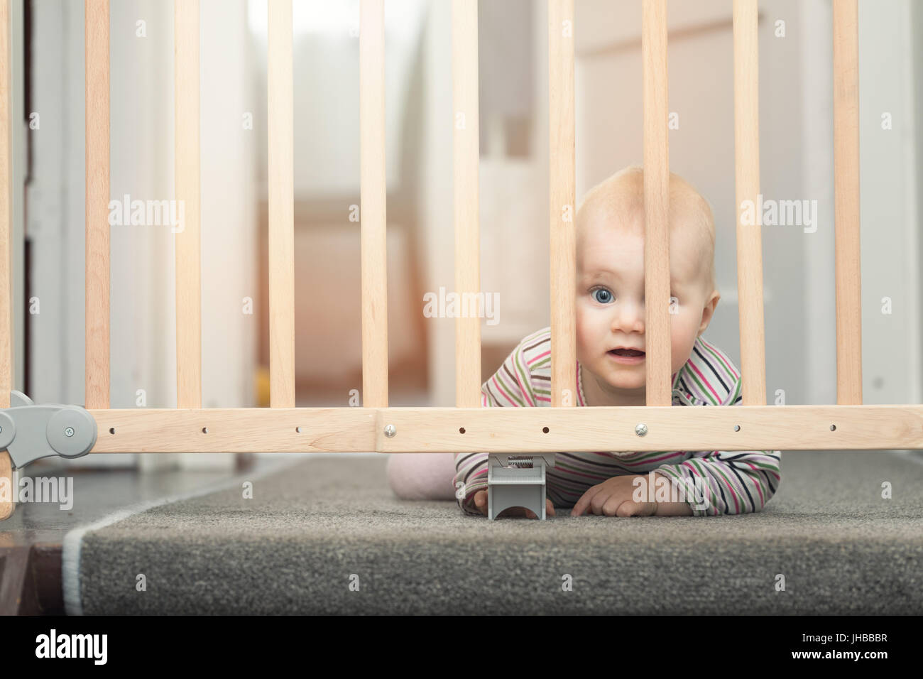 Baby dietro i cancelli di sicurezza anteriore di scale a casa Foto Stock