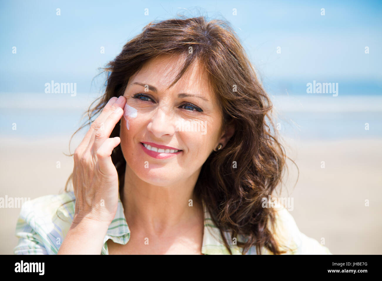 Bella donna di mezza età l'applicazione di crema di protezione solare sulla faccia sulla spiaggia Foto Stock