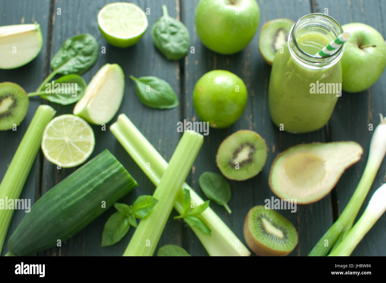 Gli ingredienti freschi intorno a un frullato verde bottiglia con paglia Foto Stock