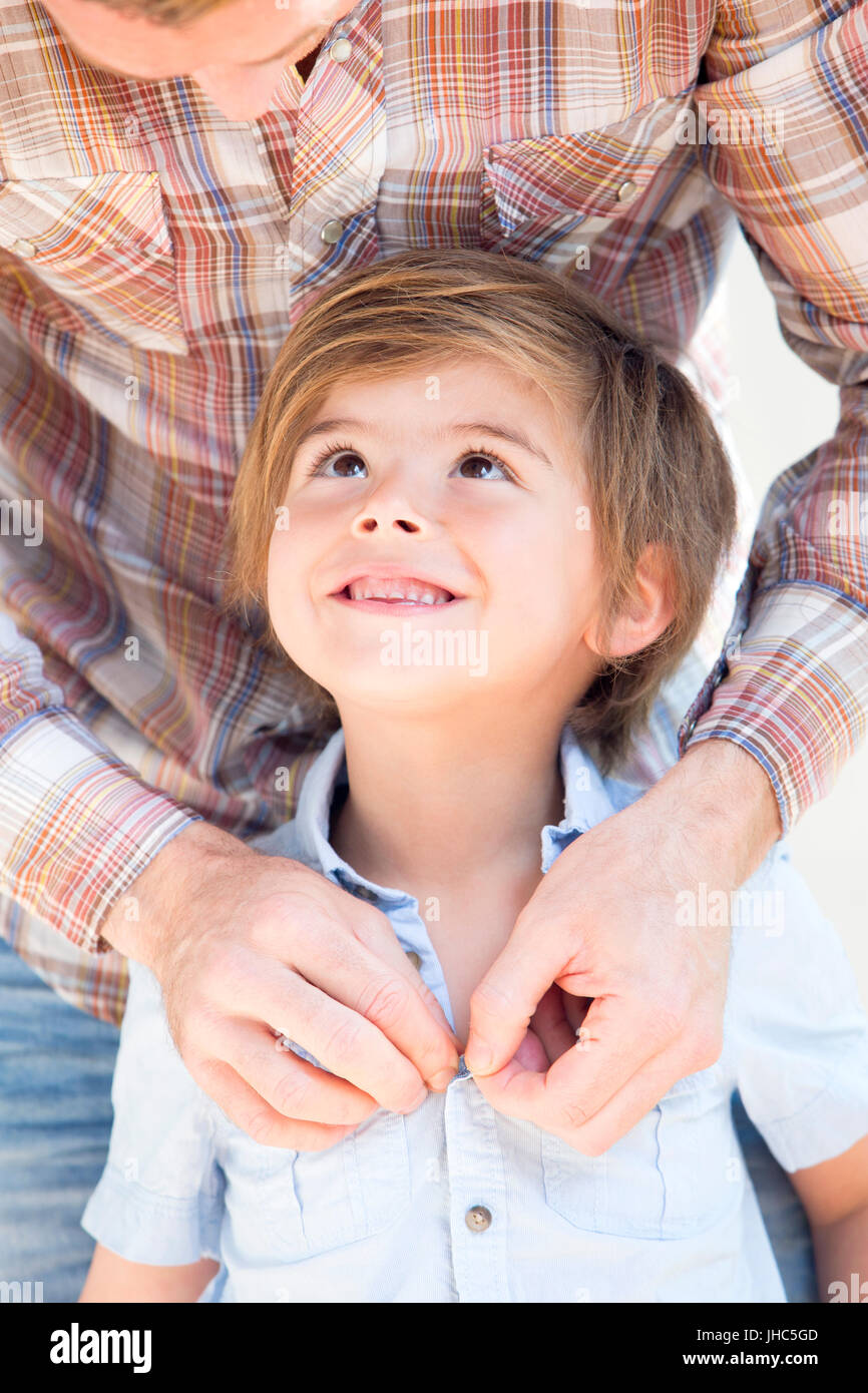 Close up di un ragazzino che sorride a suo padre mentre lui tasti su la sua maglietta per lui. Foto Stock