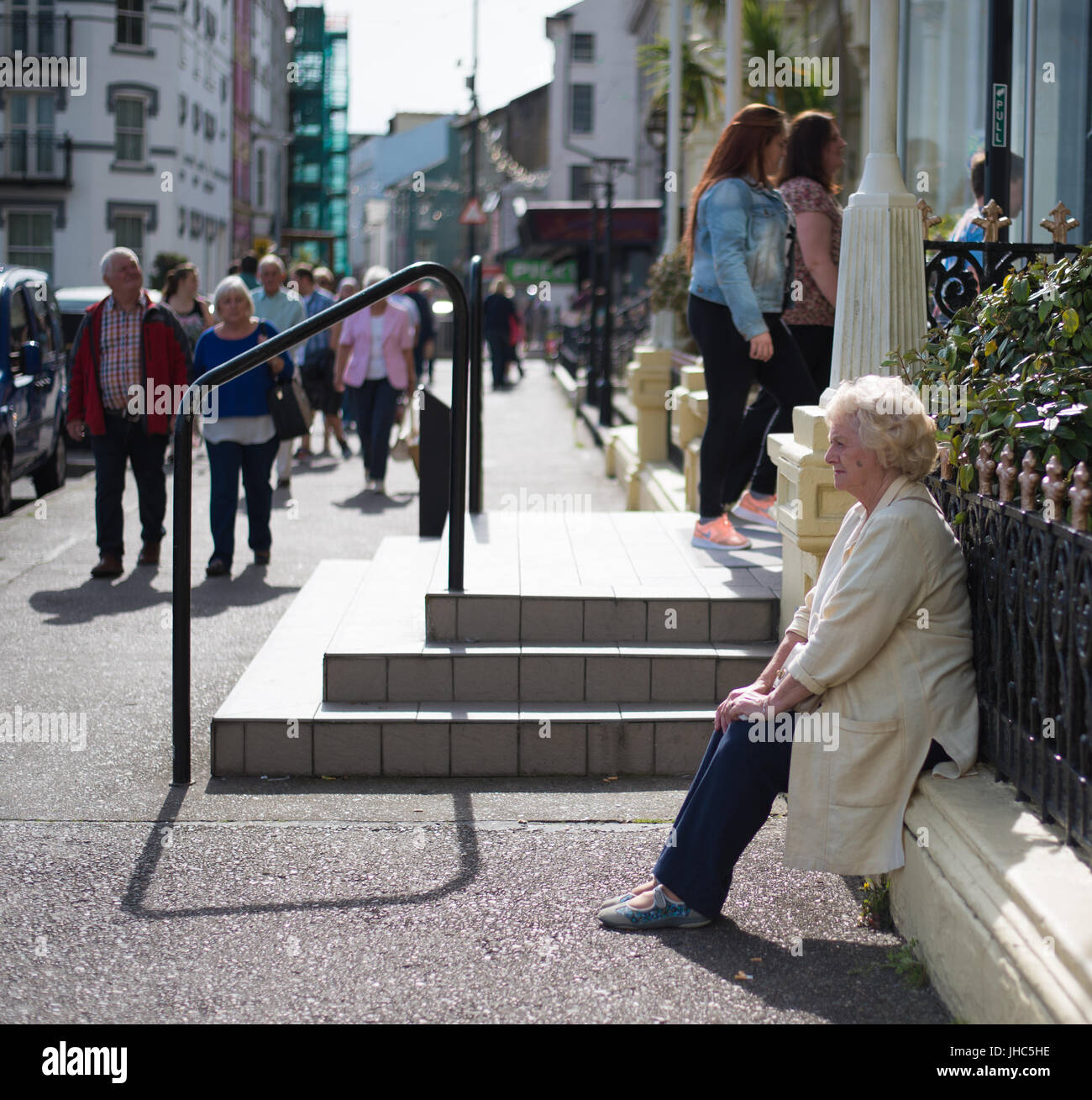 Old Lady seduti su un muretto, strada trafficata in Douglas Foto Stock