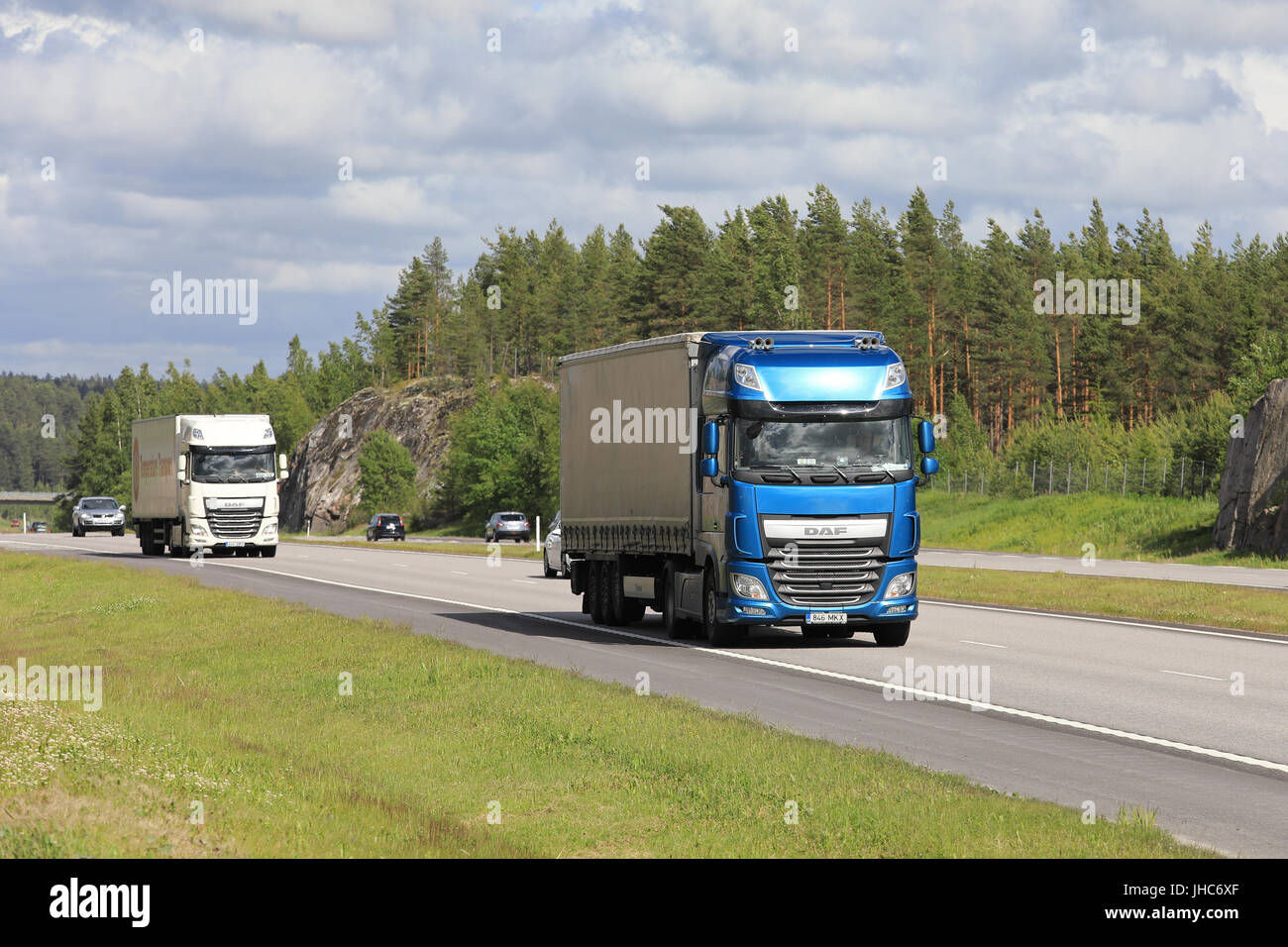Blu e bianco DAF XF semi rimorchio camion trasporto merci lungo l'autostrada tra il traffico di una bella giornata d'estate. Foto Stock