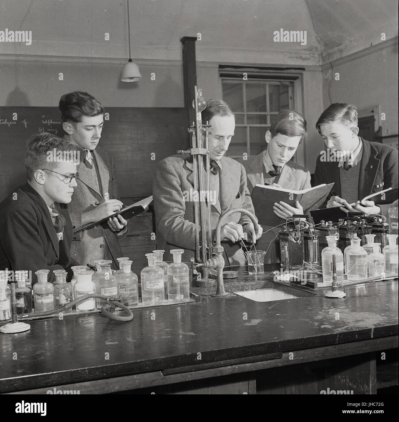 Degli anni Cinquanta, storico, post-guerra in Inghilterra, Regno Unito, Science Laboratory di Mill Hill School, a nord di Londra, Inghilterra, Regno Unito, un tradizionale britannica a pagamento solo boys Boarding School. La figura mostra i ragazzi tenendo note come l'insegnante maschio dimostra a loro come le diverse sostanze chimiche reagiscono quando miscelati insieme. Foto Stock