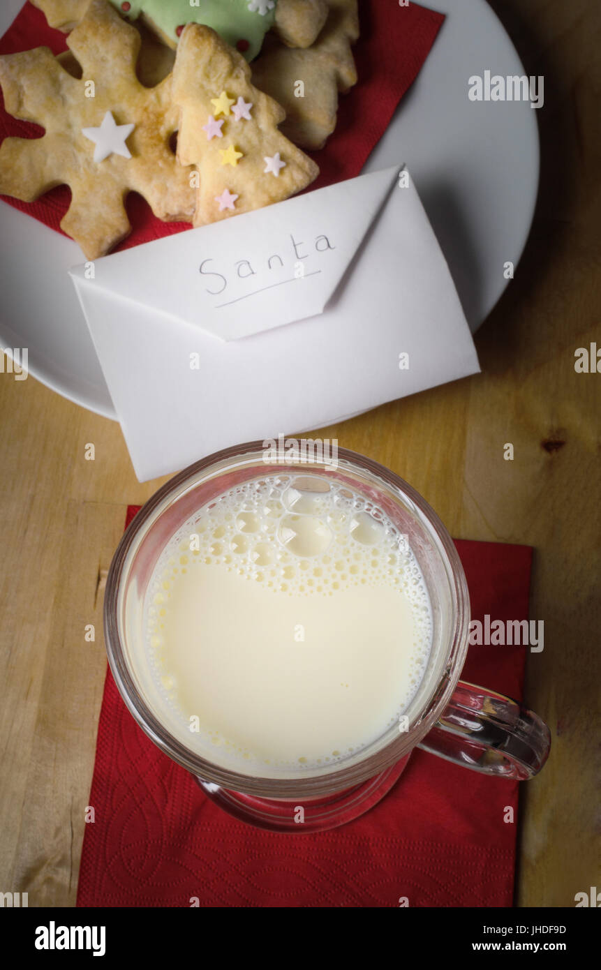 La notte di Natale in scena con una piastra di decorate biscotti) e un bicchiere di latte con busta indirizzata a Santa su un tavolo di legno. Foto Stock