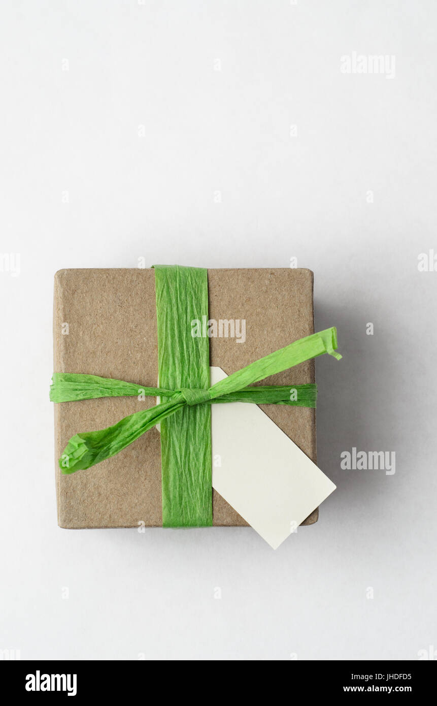 Scatto dall'alto di un semplice marrone confezione regalo con rafia verde nastro ed etichetta vuota su sfondo bianco. Foto Stock