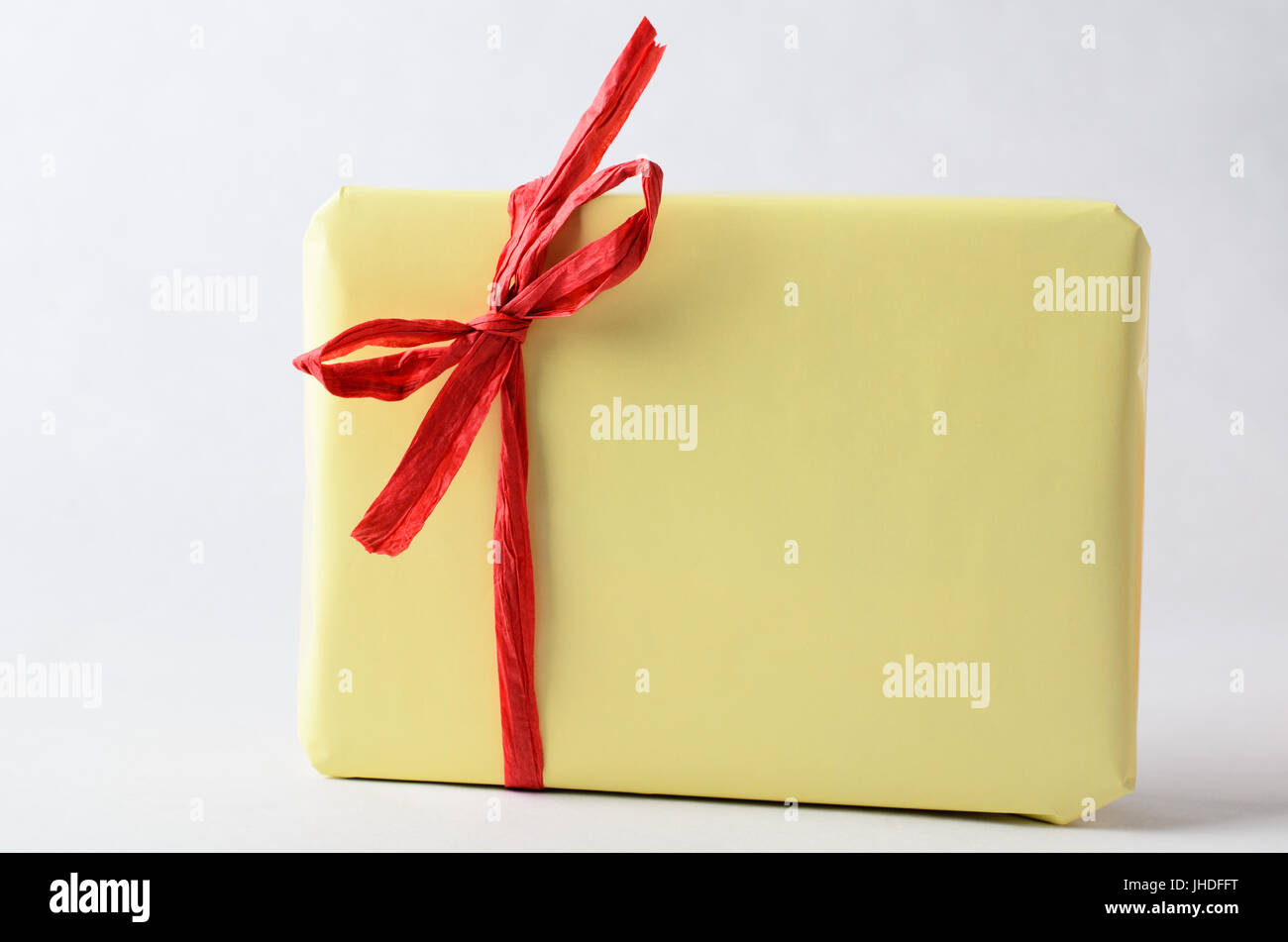 Un pacchetto regalo, molto semplicemente avvolto in formato carta gialla con rafia rossa nastro legato ad un arco. Nessuna etichetta. Copia dello spazio sul confezionamento e background. Foto Stock