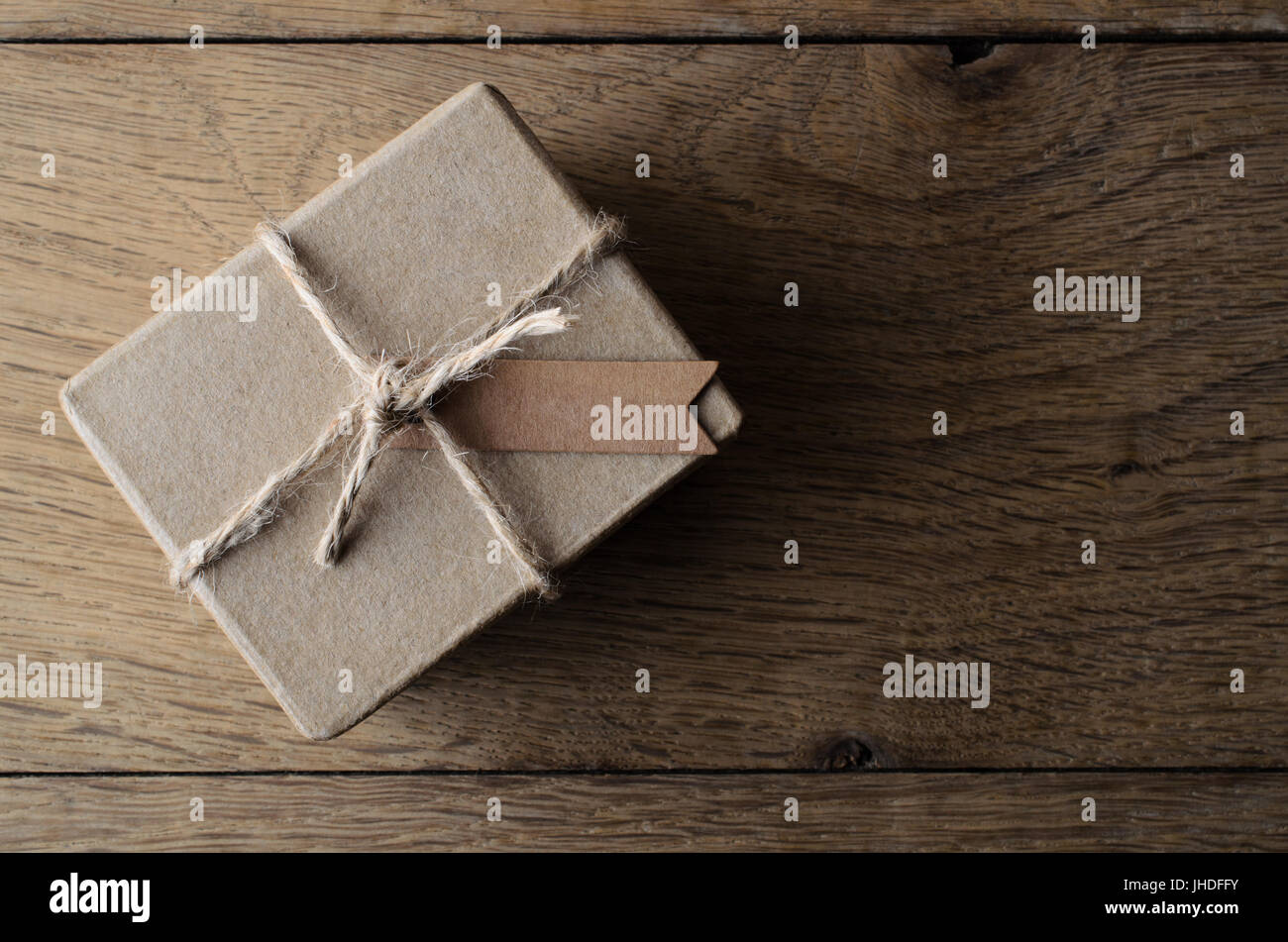 Scatto dall'alto di un semplice e rustico, marrone normale scatola regalo, legato con una corda e un tag vuoto per copia di spazio impostata sulla vecchia quercia tavolato di legno. Foto Stock