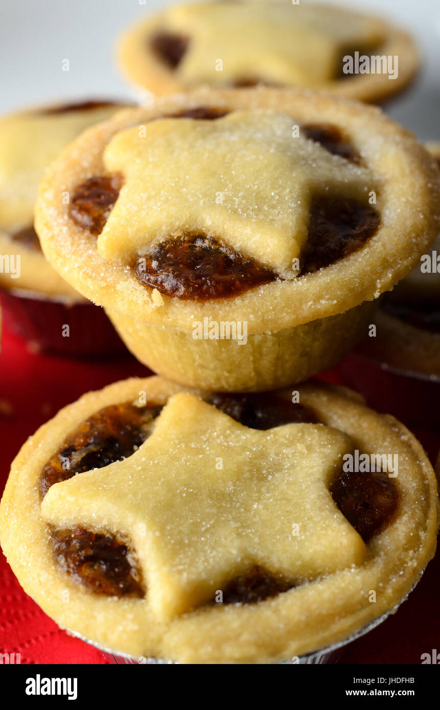 Close up di Natale pasticci di carne macinata con stella topper pasticceria, impilati su una piastra bianca con le briciole; un tovagliolo rosso. Foto Stock