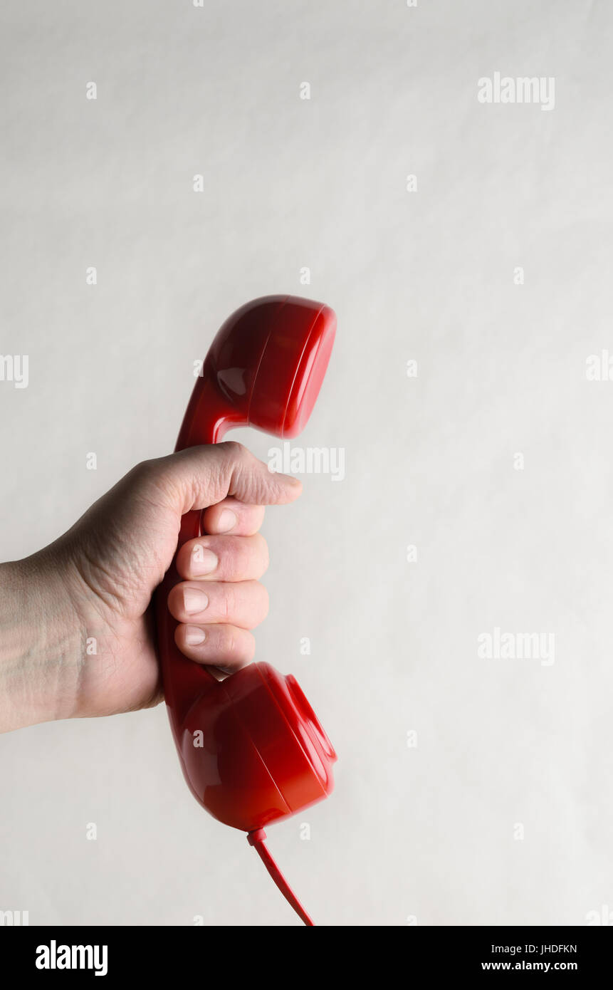 Vista laterale di un retro rosso ricevitore telefonico, tenuto in una mano maschile come se il superamento di una chiamata per qualcuno. Off sfondo bianco fornisce la copia dello spazio. Foto Stock