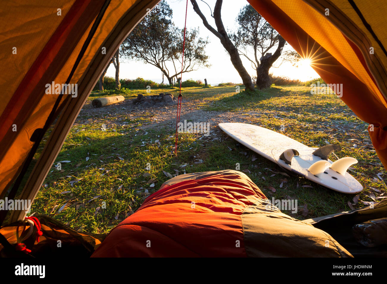 Una persona in un sacco a pelo con un bel punto di vista da una tenda come la luce del mattino illumina il campeggio e la circonda. Foto Stock