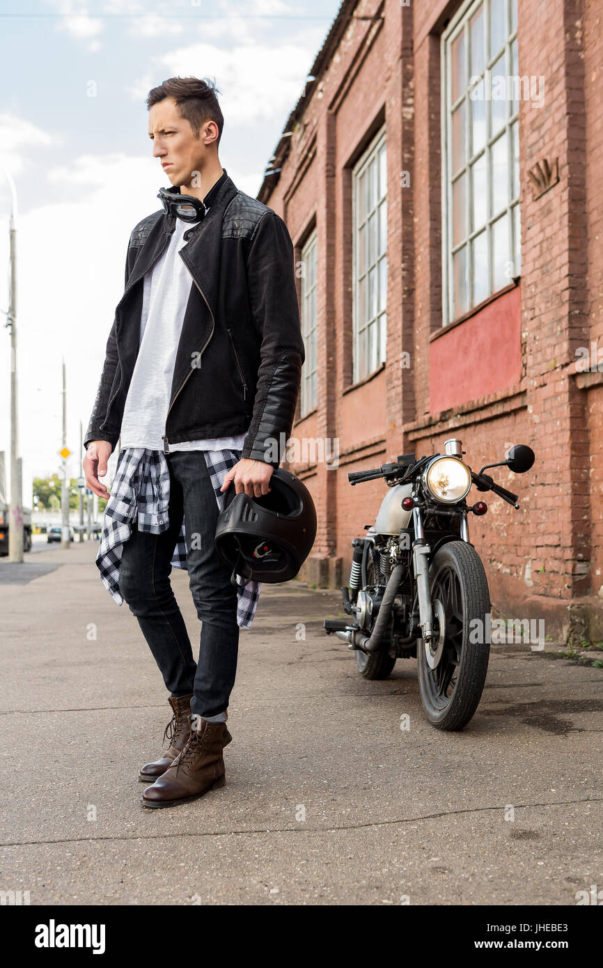 Bello rider biker man in black giacca di pelle e casco a piedi dal classico  stile Café Racer motocicletta. Moto custom made in vintage garage. Br Foto  stock - Alamy